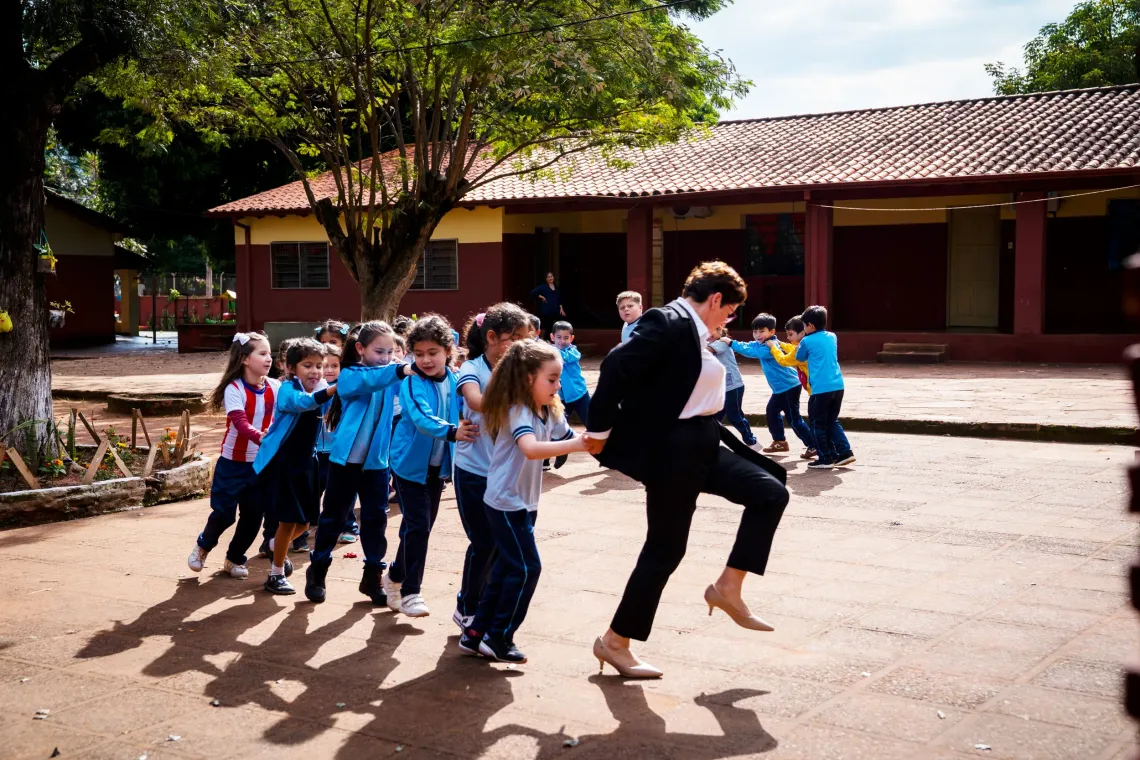 Estudiantes participan en una actividad grupal en el patio de la escuela, acompa&ntilde;ados por su maestra durante una din&aacute;mica recreativa.