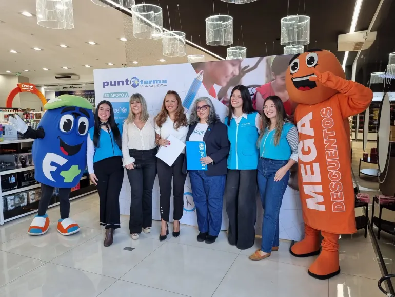 6 personas, representantes de UNICEF y Punto Farma posan abrazadas con las botarga de la farmacia