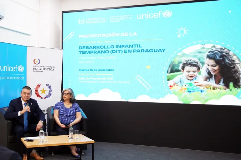 Director del INE y Representante de UNICEF sentados en el escenario, de fondo una pantalla que muestra la portada del documento