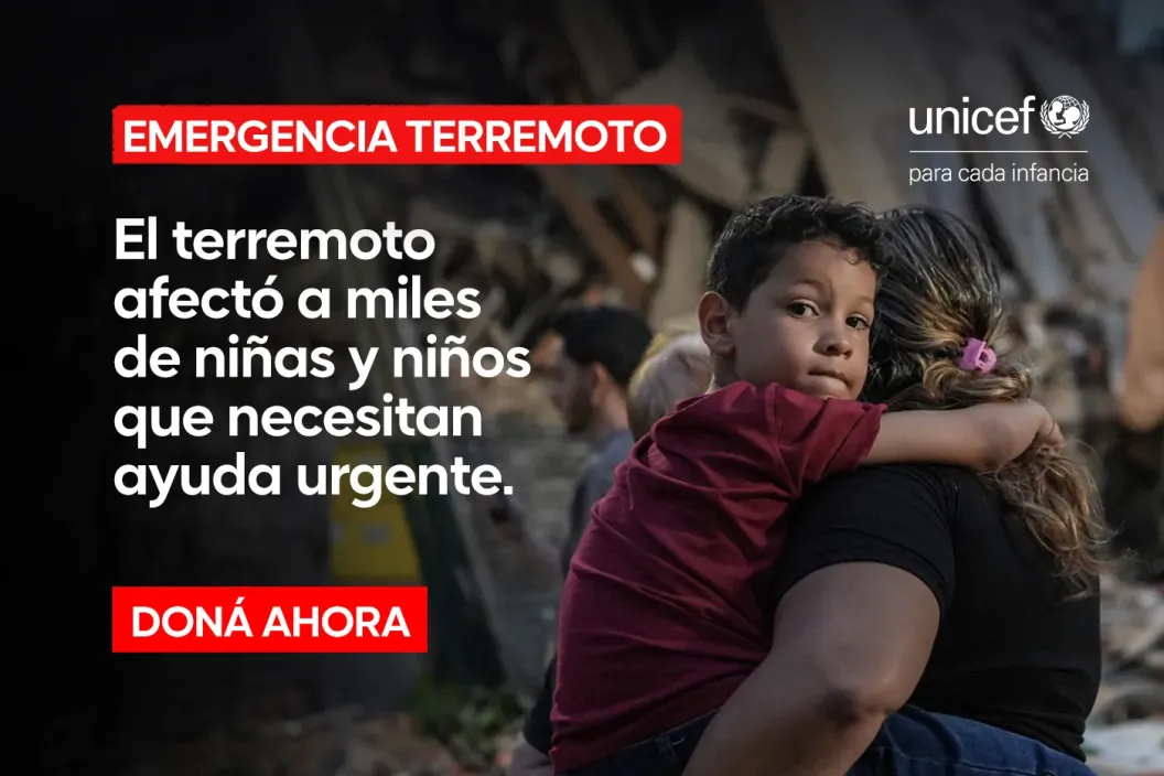 Ni&ntilde;o en los brazos de su madre, en el fondo se ven edificios afectados por el terremoto