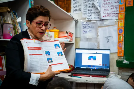 Docente utiliza materiales impresos y una computadora port&aacute;til para desarrollar una actividad educativa en el aula.
