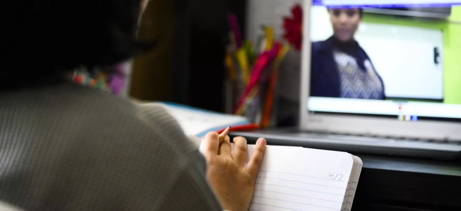Girl taking notes during an online class on her computer at home 