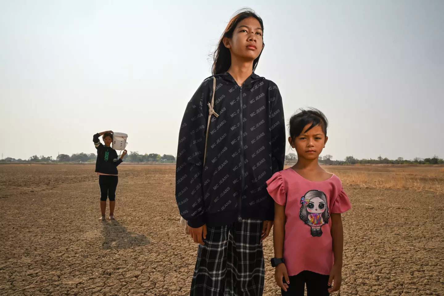 Children walking across cracked, salty soil, where locals dig up the earth to boil salt for sale.