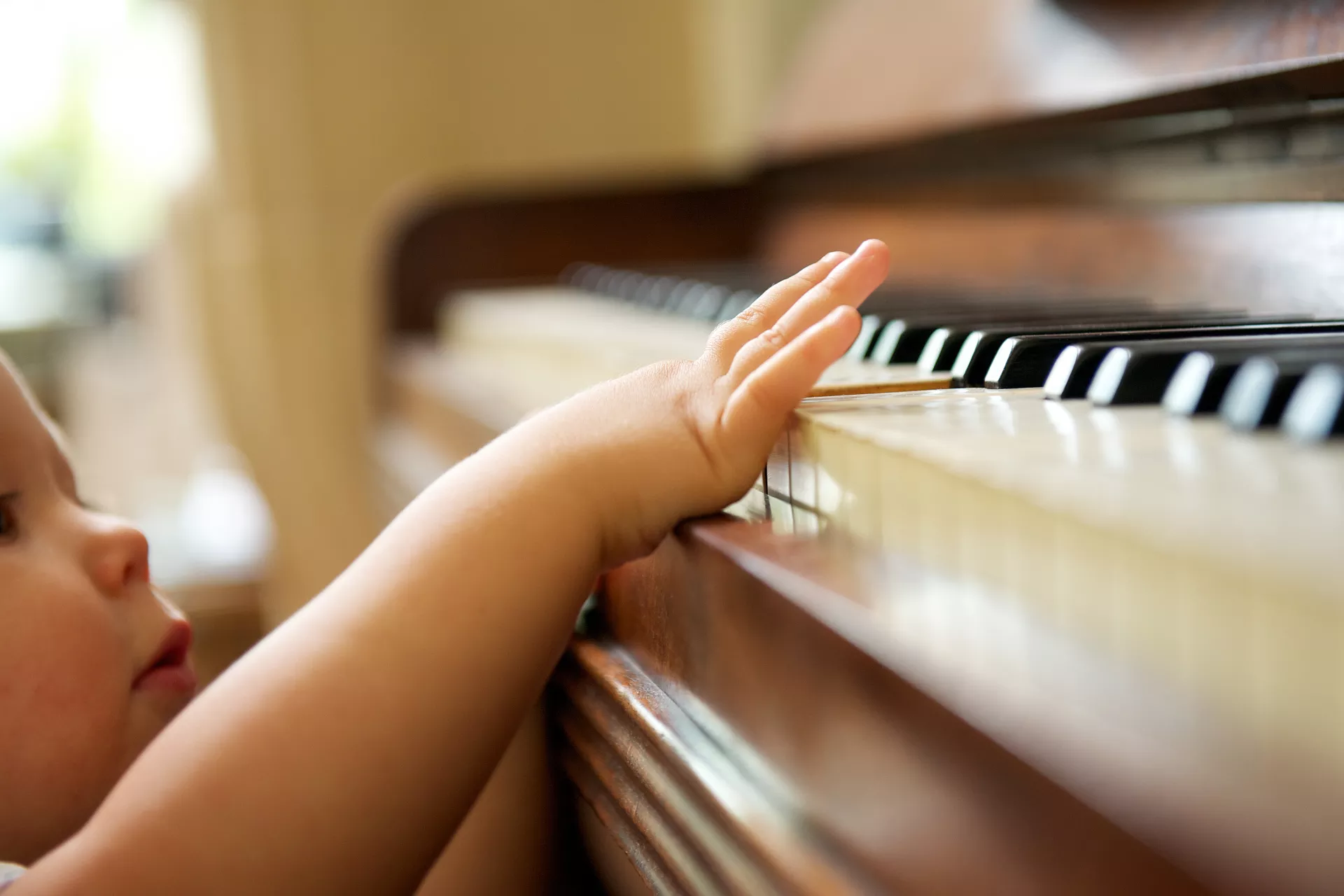 A toddler reaches up to touch keys on a piano.