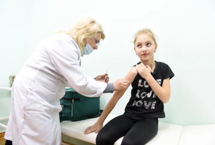 Une agente de sant&eacute; portant une blouse blanche vaccine une petite fille v&ecirc;tue d'un t-shirt noir. 