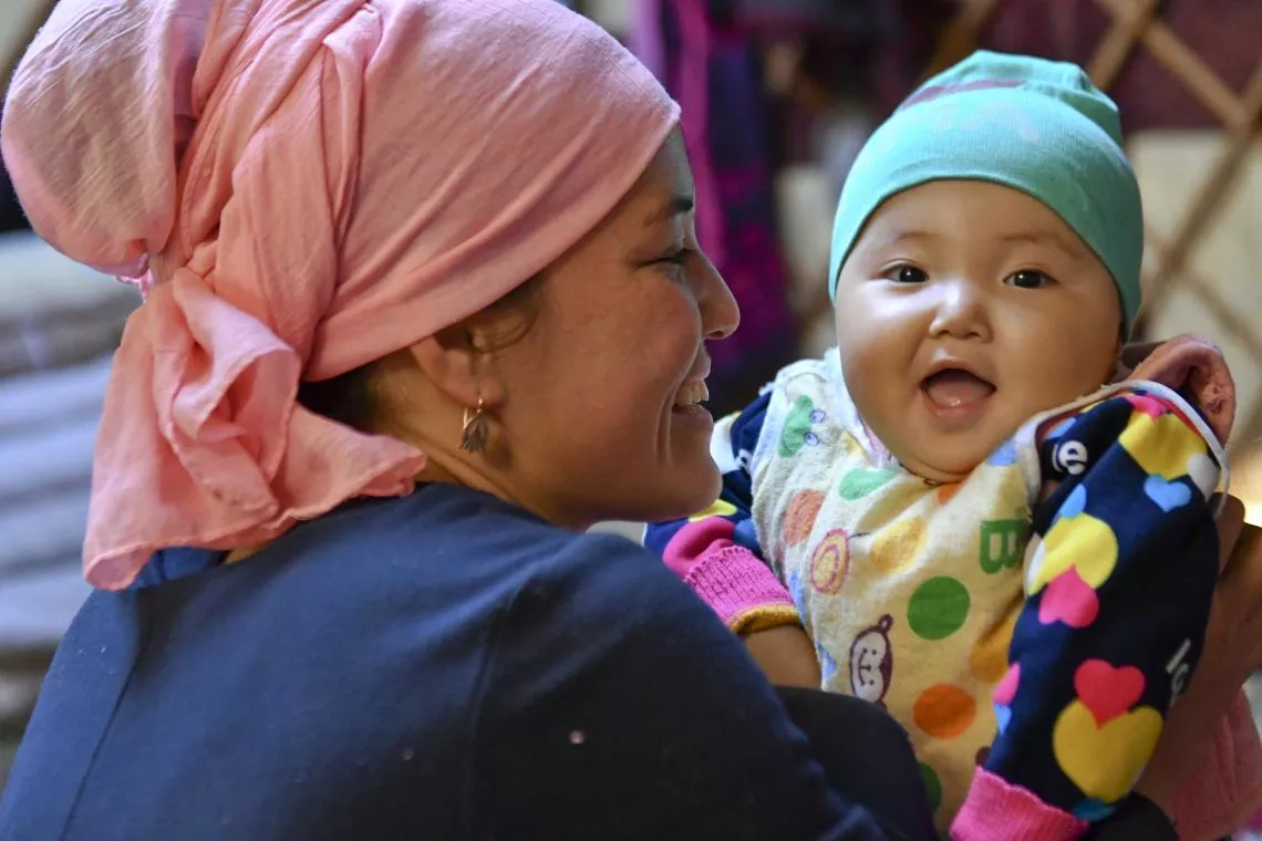 A girl smiles as she is held by her mother in Kyrgyzstan.