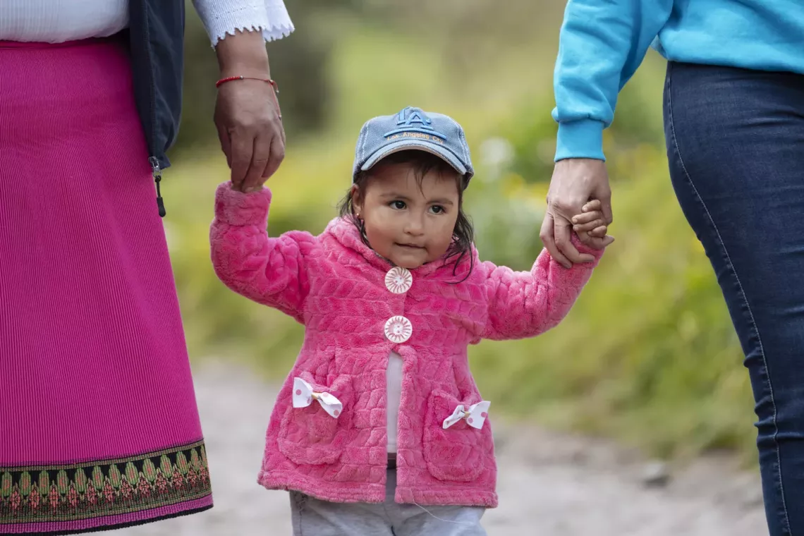 In Turugucho, Ecuador, 2-year-old Aysel Yanez walks down a road holding hands with Mar&iacute;a Ortencia Catucuago (left), the local Community Watcher, and Katherine Silva, Health and Nutrition Officer at UNICEF Ecuador.