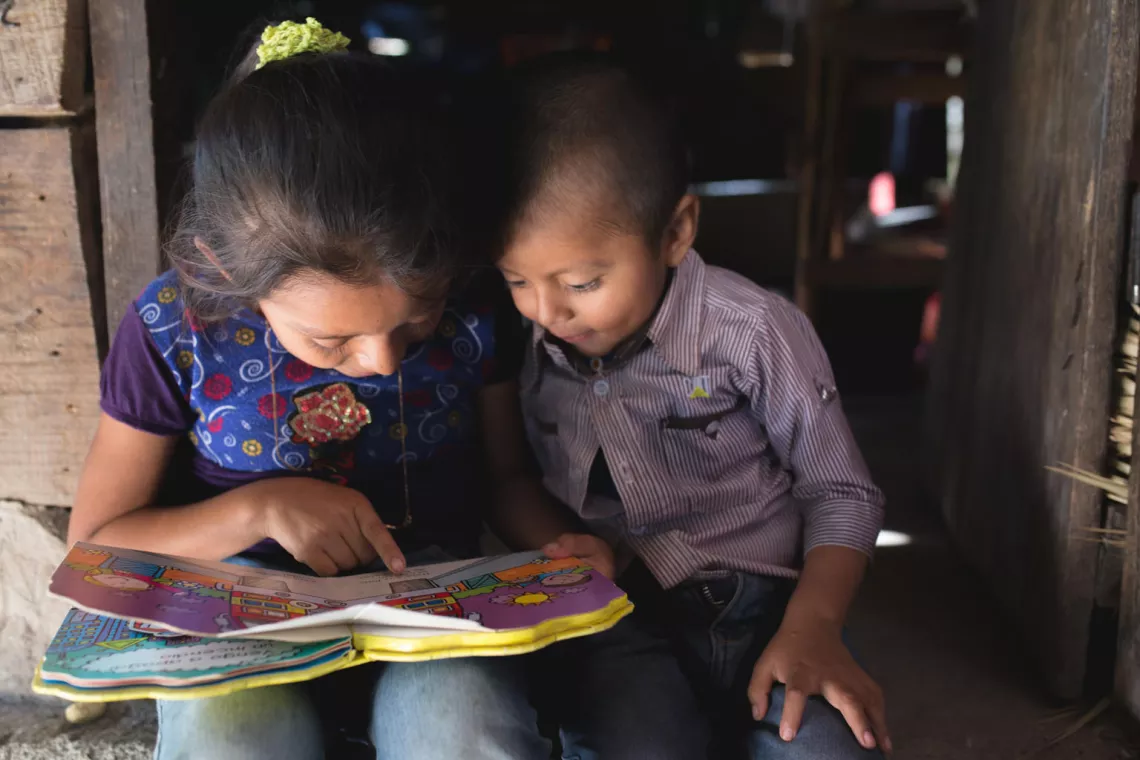 Une petite fille apprend à son frère à lire.