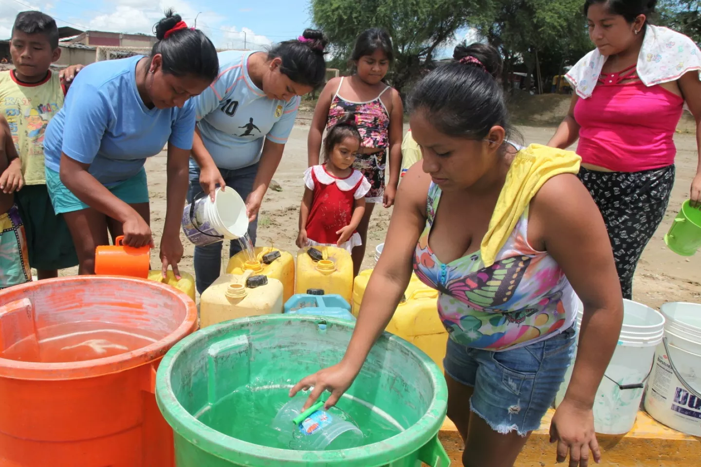 Mujeres recogen agua de baldes, mientras ni&ntilde;os miran desde atr&aacute;s