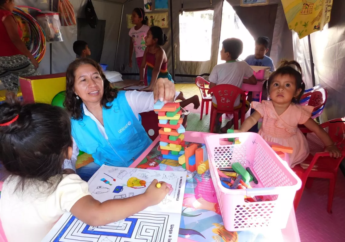 Una mujer comparte juegos con ninos y ninas dentro de una carpa