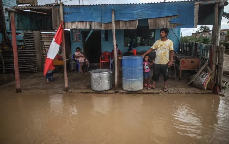 Familia de pie frente a casa inundada, con bandera de Peru.