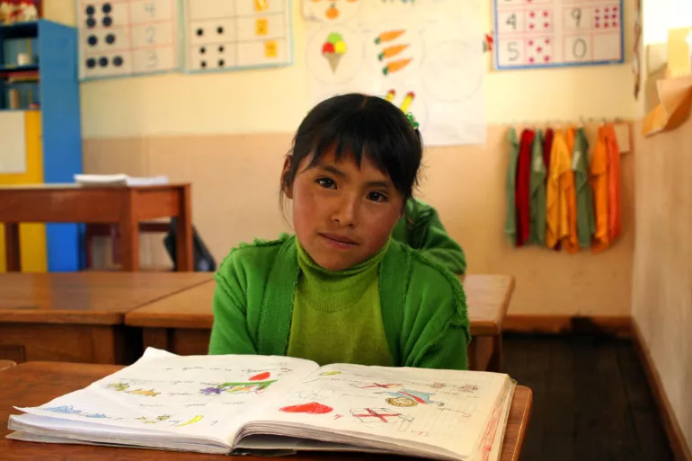 Una ni&ntilde;a sentada en su pupitre, dentro del sal&oacute;n de clase, con un cuaderno abierto.