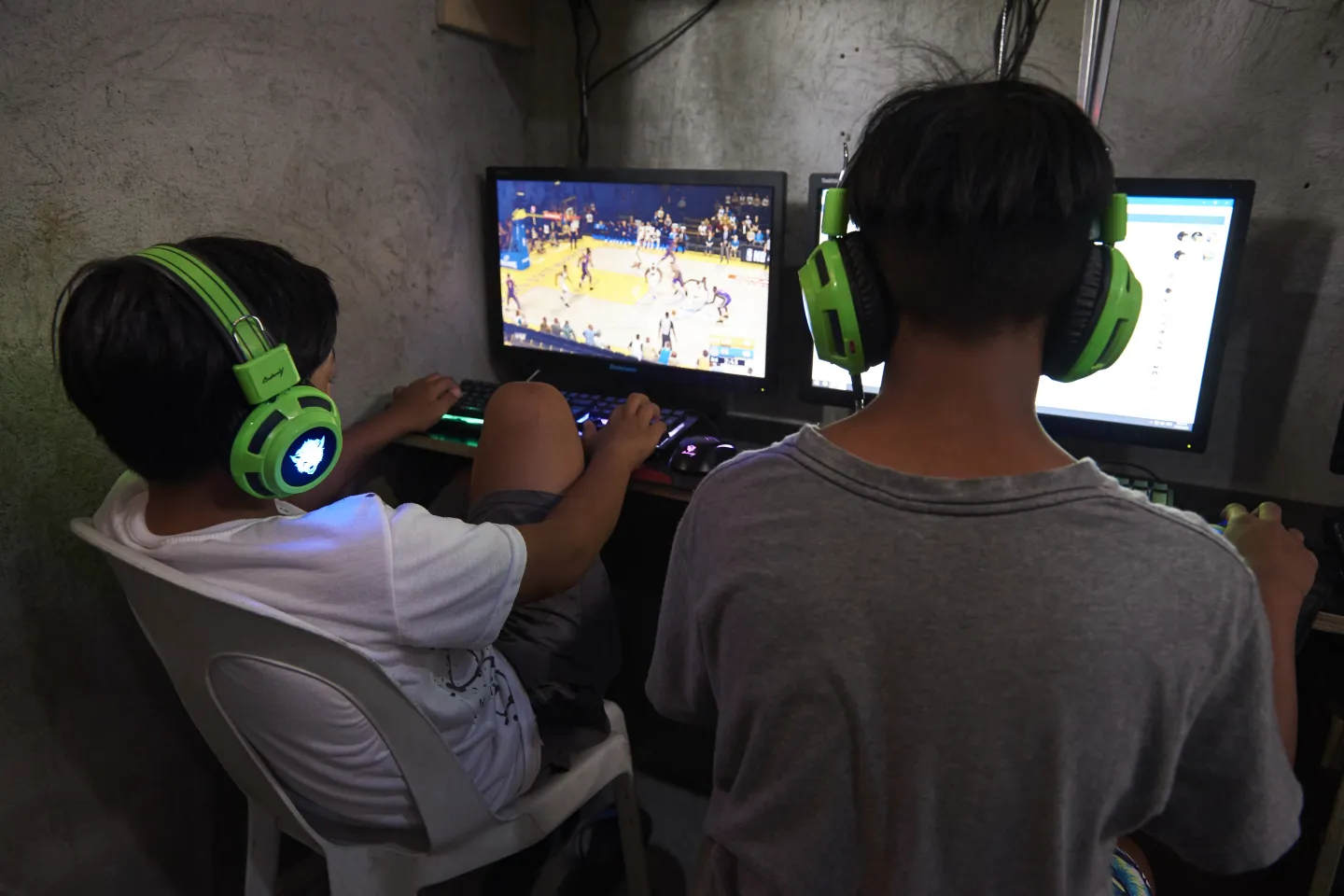 Two children playing games inside a public computer rental shop. Their faces are turned away from the camera, hiding their identities