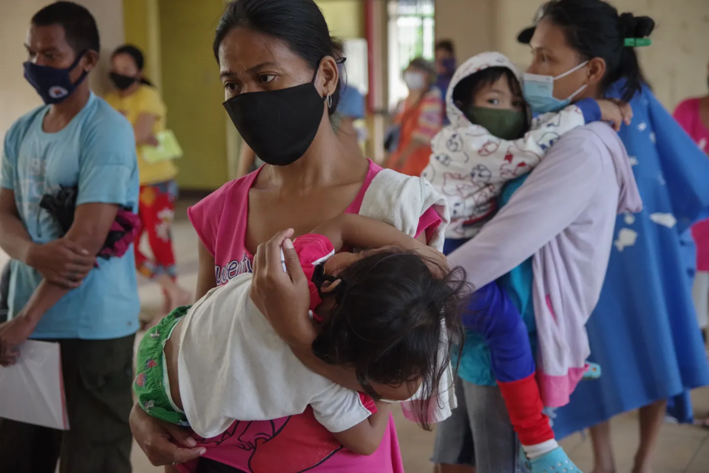 Parents and caregivers carrying their young children in an evacuation center. Most of them are wearing face masks.