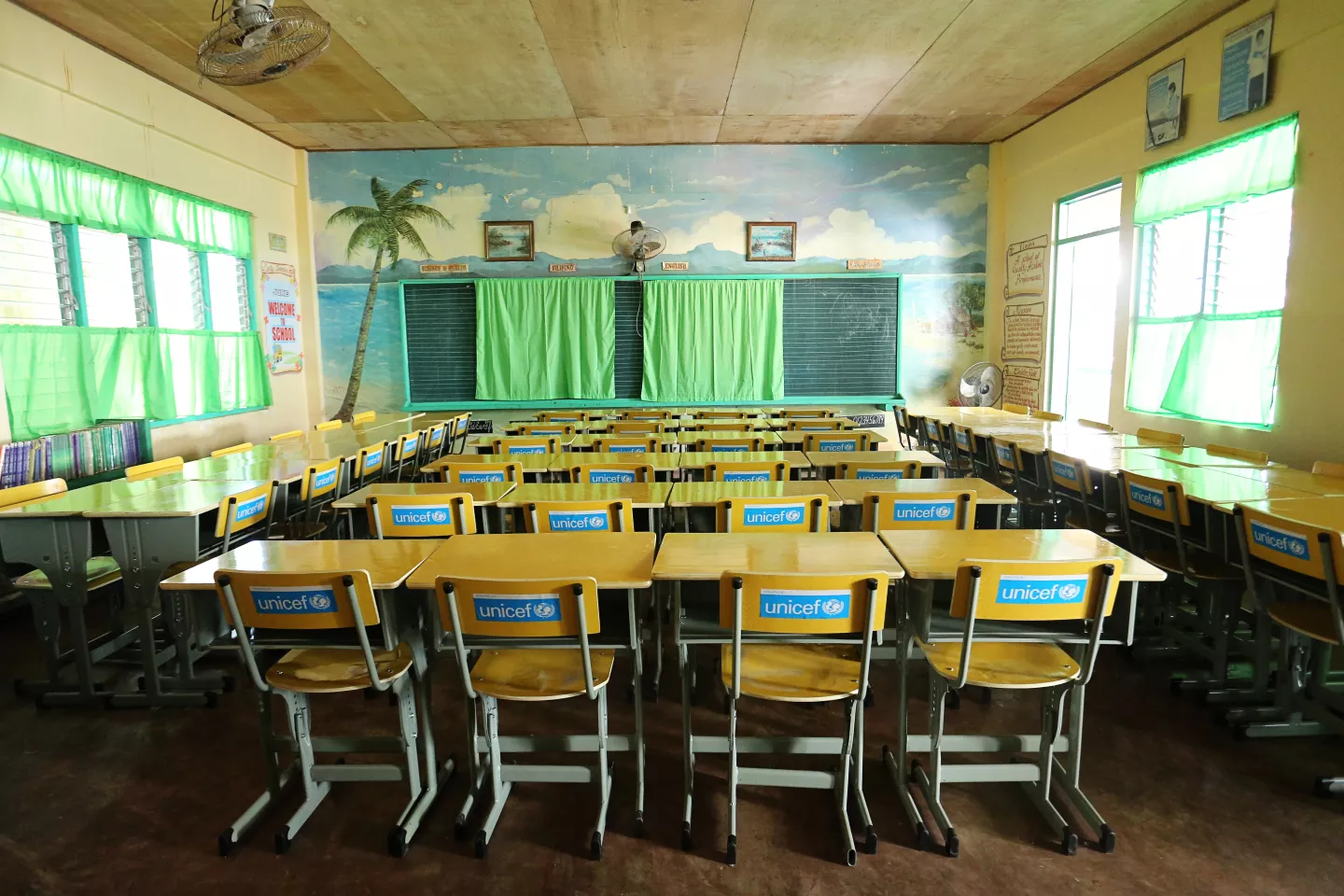 An empty classroom. The backs of the chairs have stickers on them with the text "Donated by UNICEF"