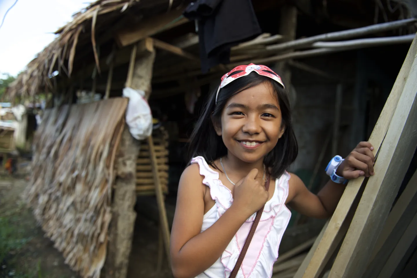 A young girl child stands outside a hut