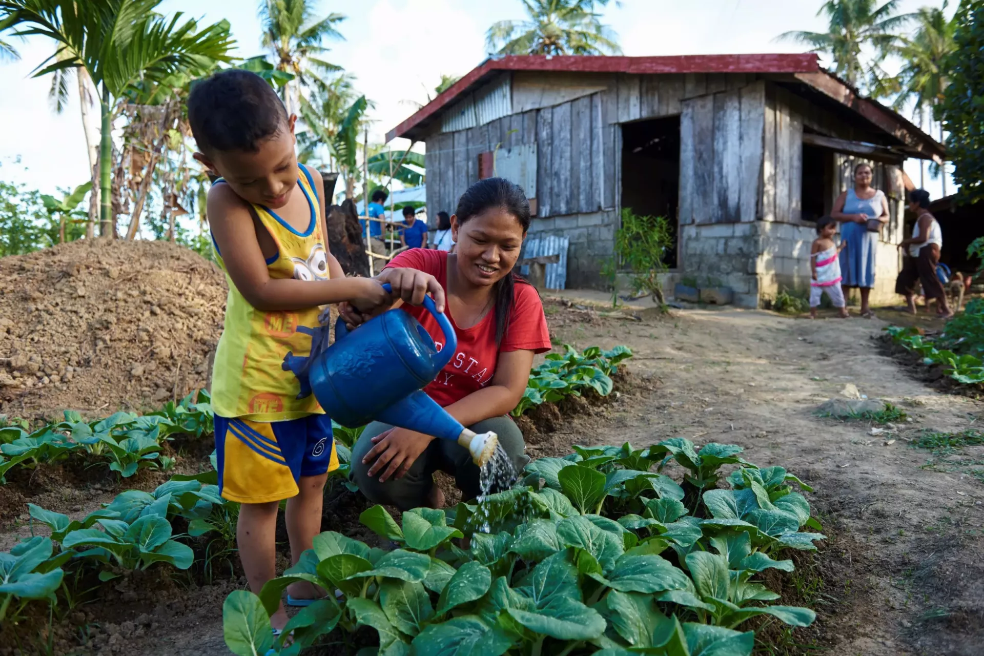 A young boy with her mom watering vegetables in their backyard