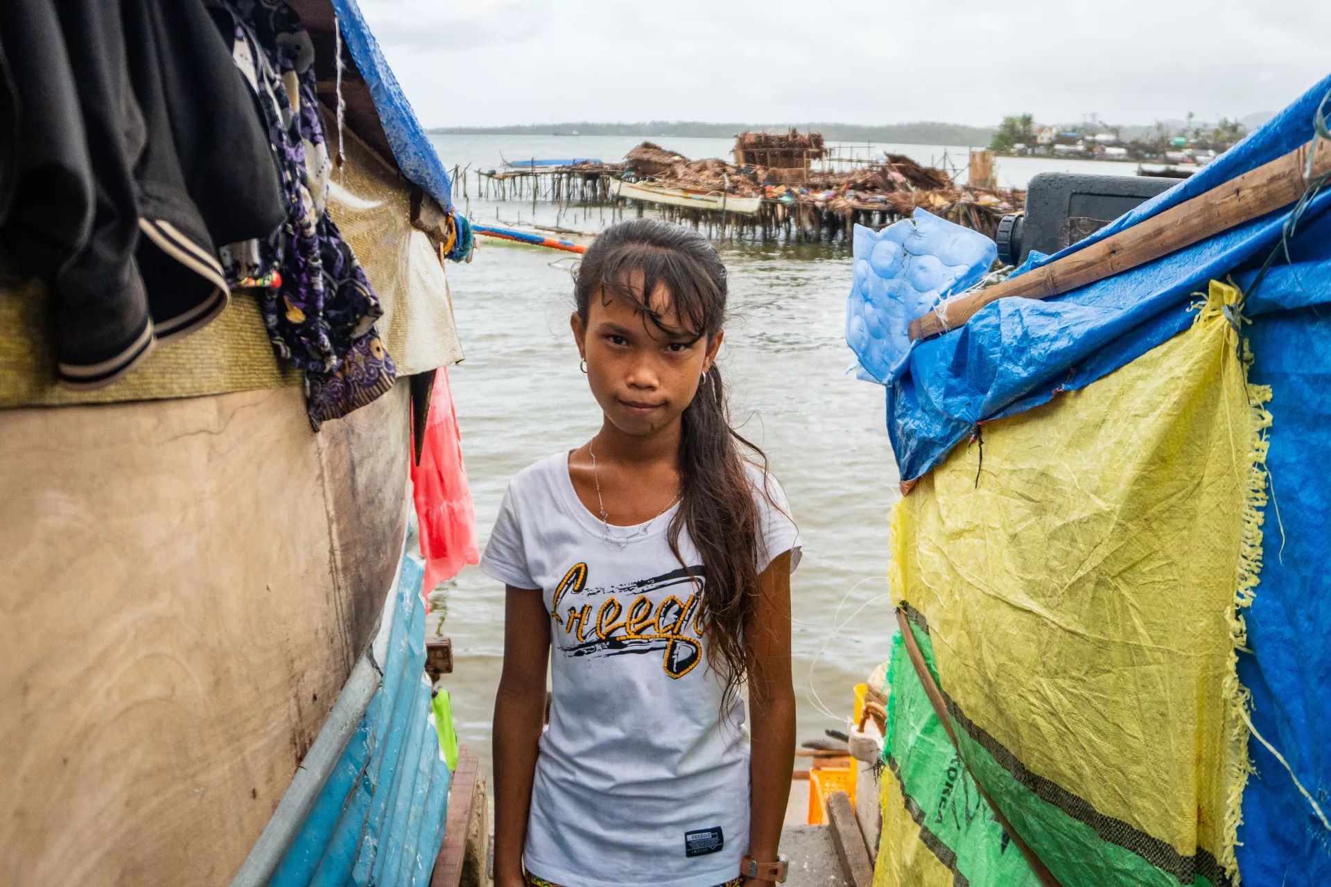 A girl stands by the water amid makeshift shelter destroyed by a typhoon