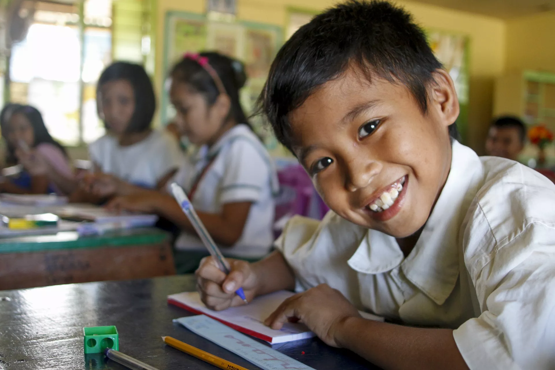 A boy smiles as he writes in class