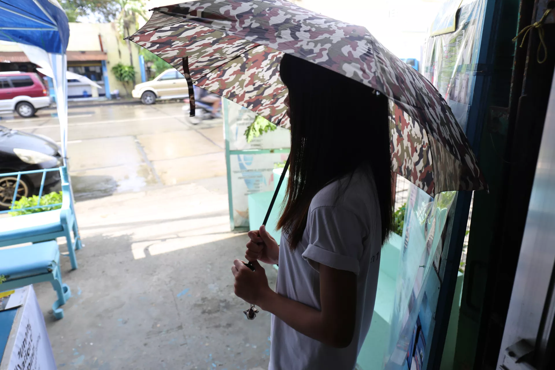A girl stands outside a health clinic holding an umbrella, with her face and identity hidden by the umbrella's shadow.