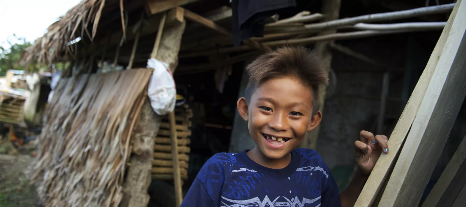 A smiling boy stands outside a hut