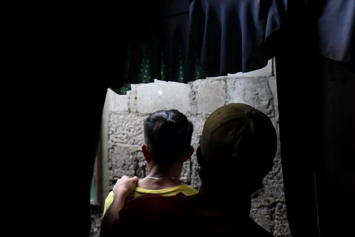 Two boys inside a darkened room, facing away from the camera