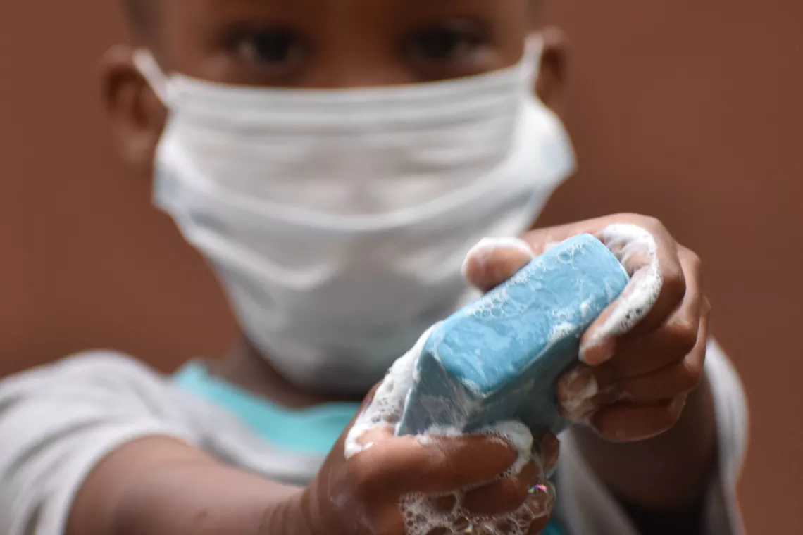 A child wearing a face mask washing their hands with soap