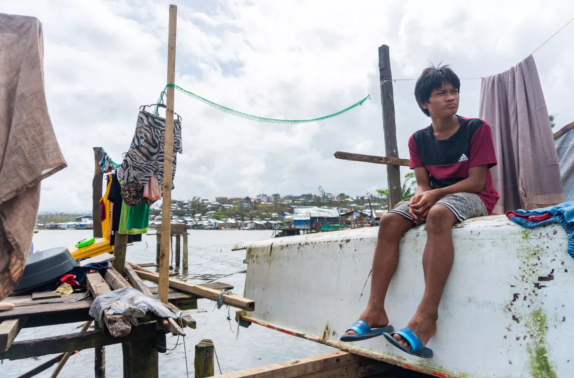 A boy sitting by the water amid debris and structures damaged by a typhoon