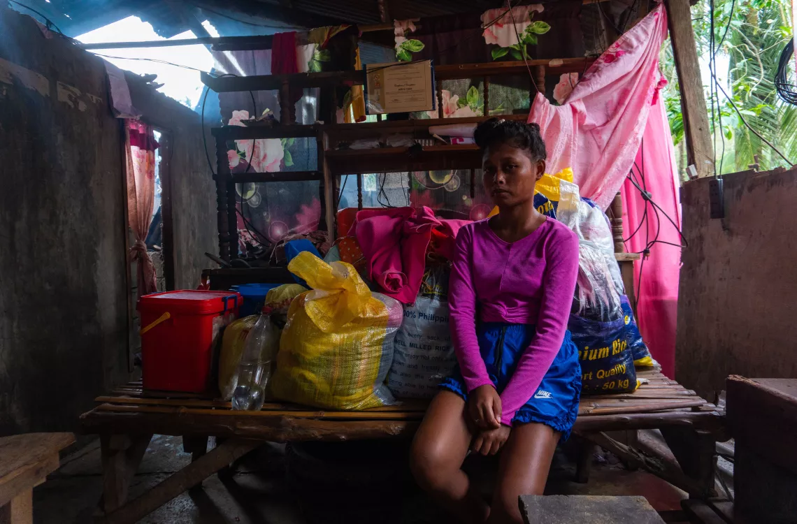 A girl sitting by their family's belongings inside a damaged house
