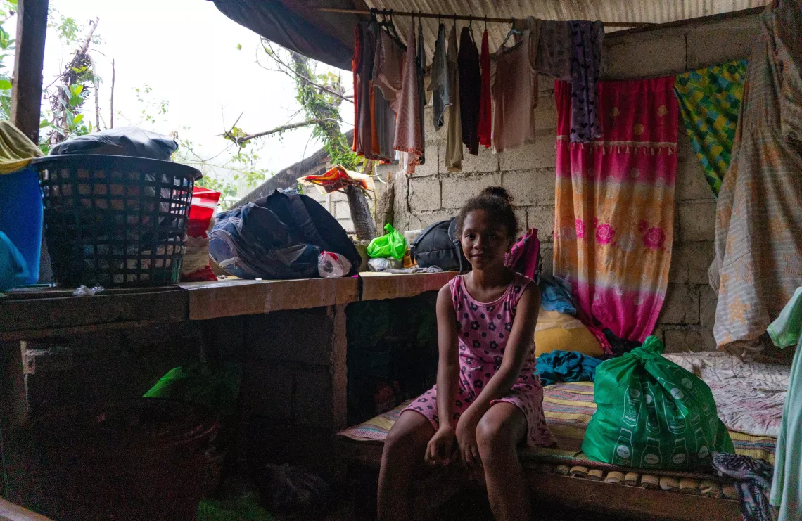 A girl sitting on a bed inside a house damaged by a typhoon