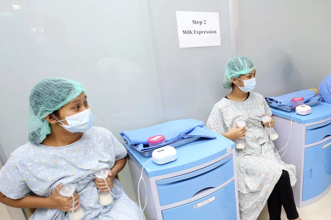 Lactating women, wearing laboratory gowns, face masks and hair caps, collect milk from their breasts by using electronic breast pumps.