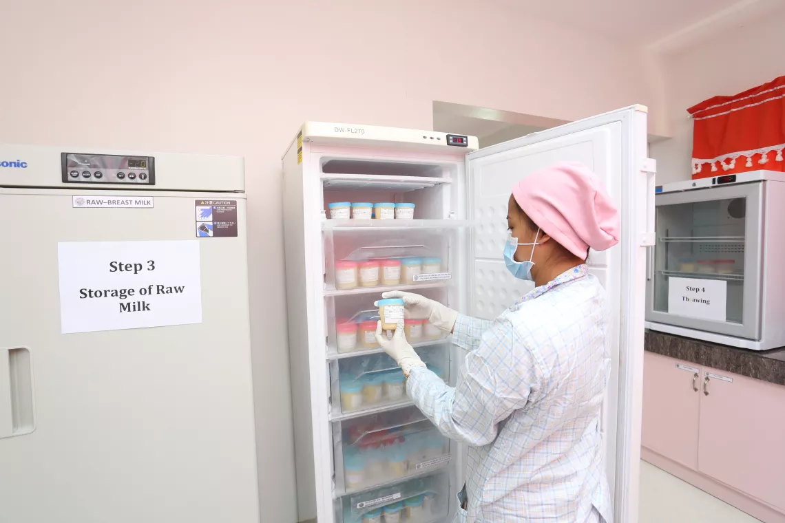 A health worker, wearing a laboratory coat, gloves, face mark and hair cap, checks breast milk stored in a refrigerator at a human milk bank.