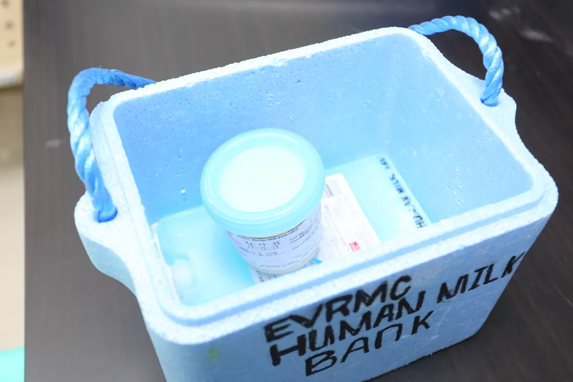 A plastic container containing breast milk inside a cooler with a gel freeze pack