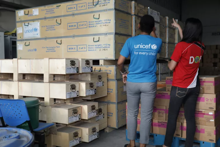 Staff members from UNICEF and the Department of Health, wearing their respective branded shirts, inspect UNICEF tents delivered to the Department of Health warehouse