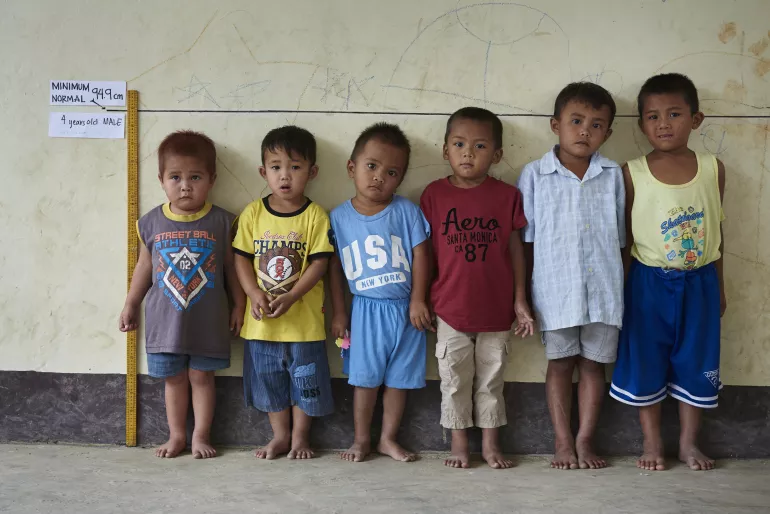 Children with different heights but of the same age line up in front of a height measurement line