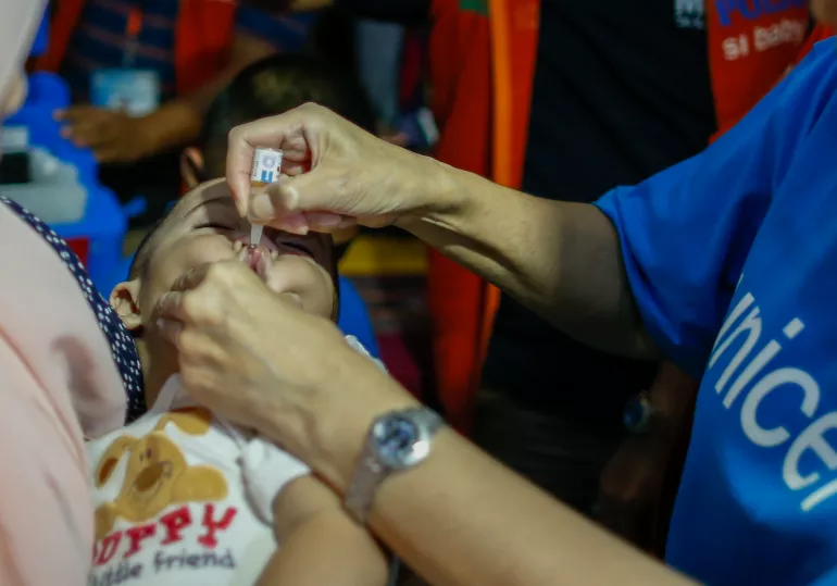 A child receives a dose of oral polio vaccine given by a UNICEF staff member