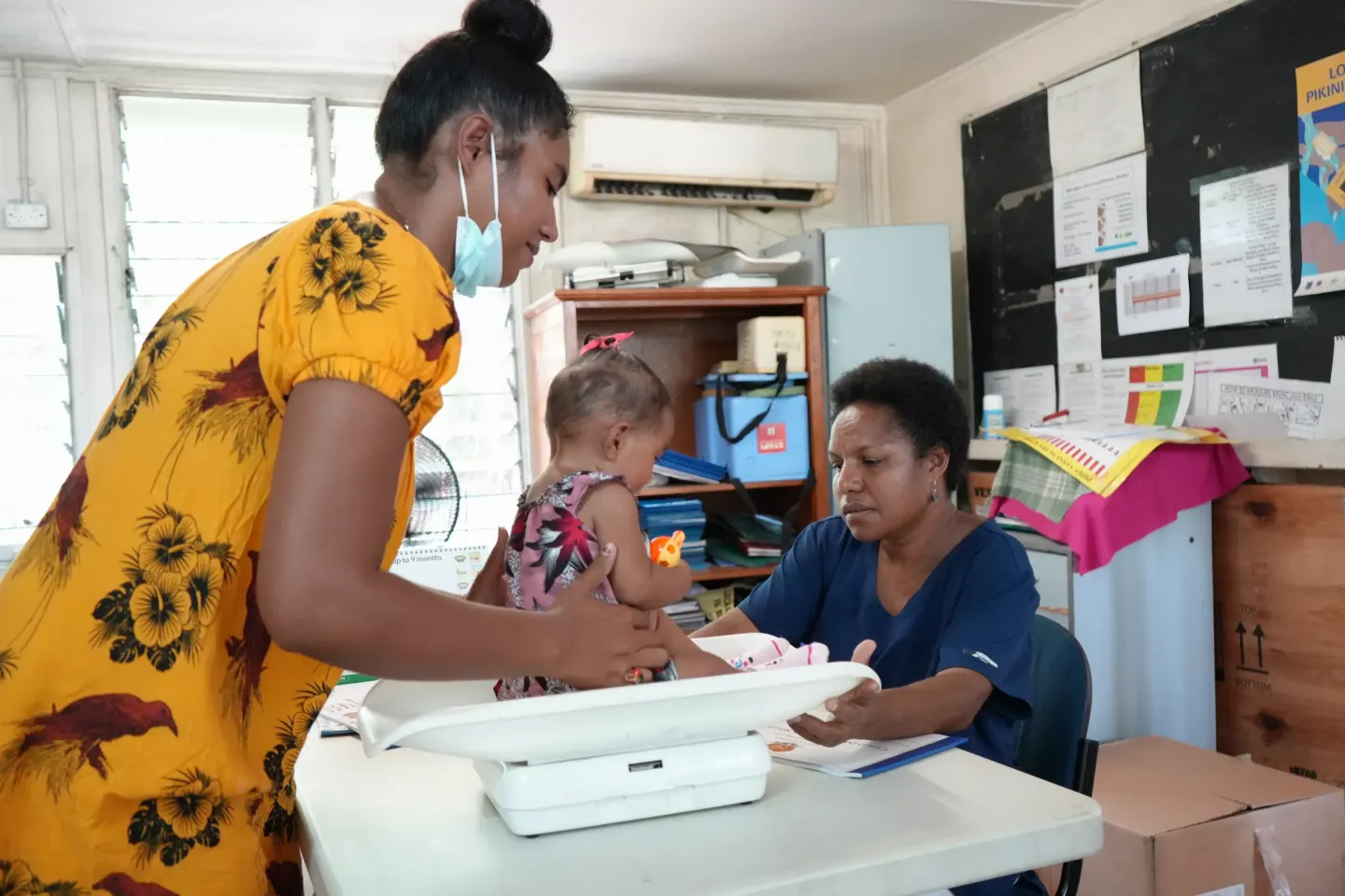 Sr. Garia Baker helps weight a baby before administering immunisation shots.