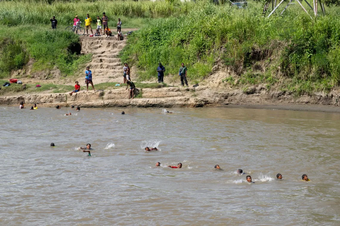 A group of school students swimming across the Kemp Welch river in Rigo District