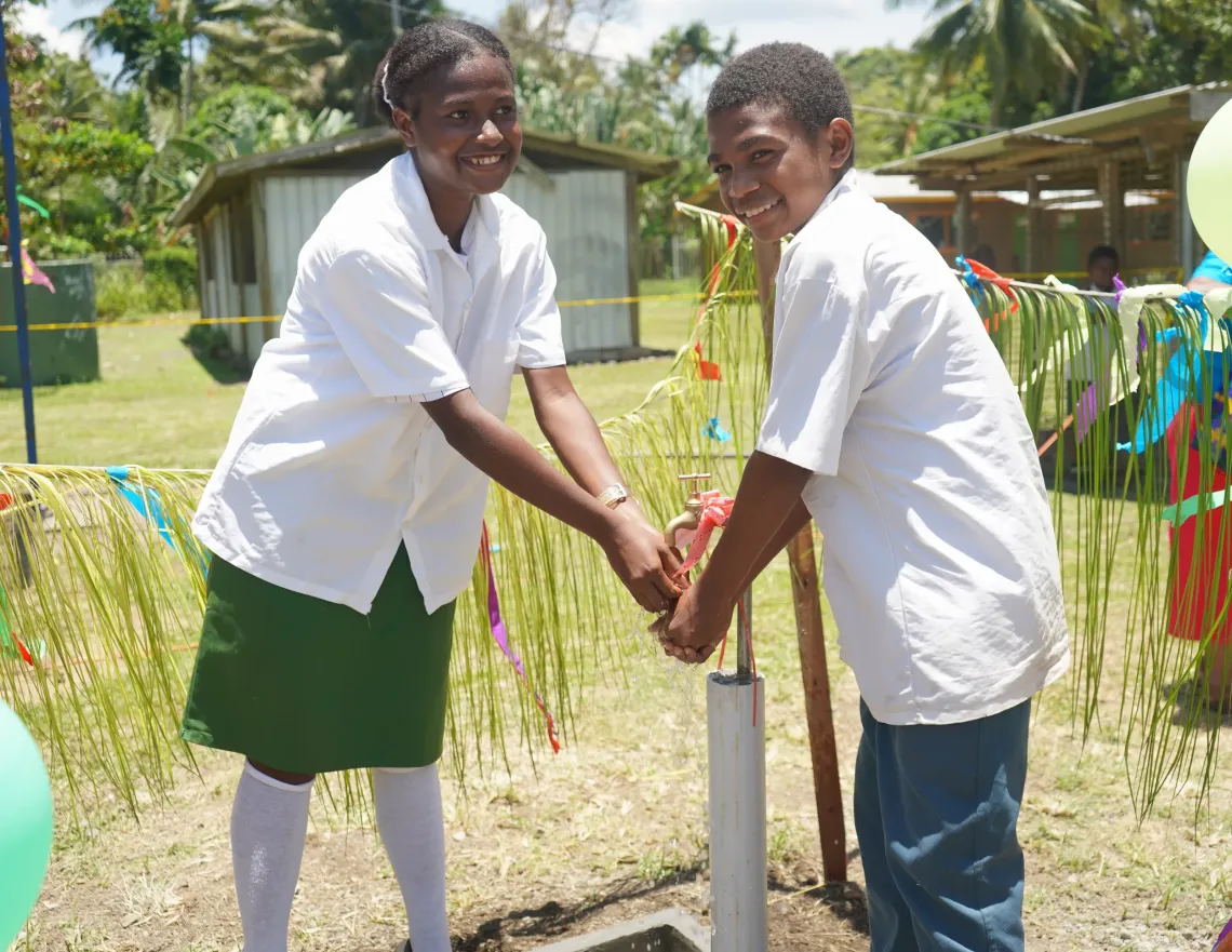 Student leaders, Gwendelene and David, use a recently installed water tap to wash their hands.