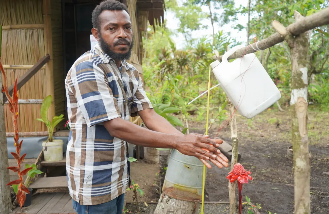 Community Motivator, Kossy Baput, washing his hands in front of a new toilet in Nasuampum community