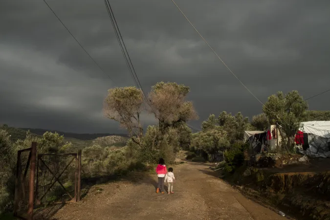 Two children walk on a dirt road surrounded by trees.