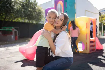 Copil și mama sa &icirc;mbrățiș&acirc;ndu-se afară &icirc;ntr-un loc de joacă.