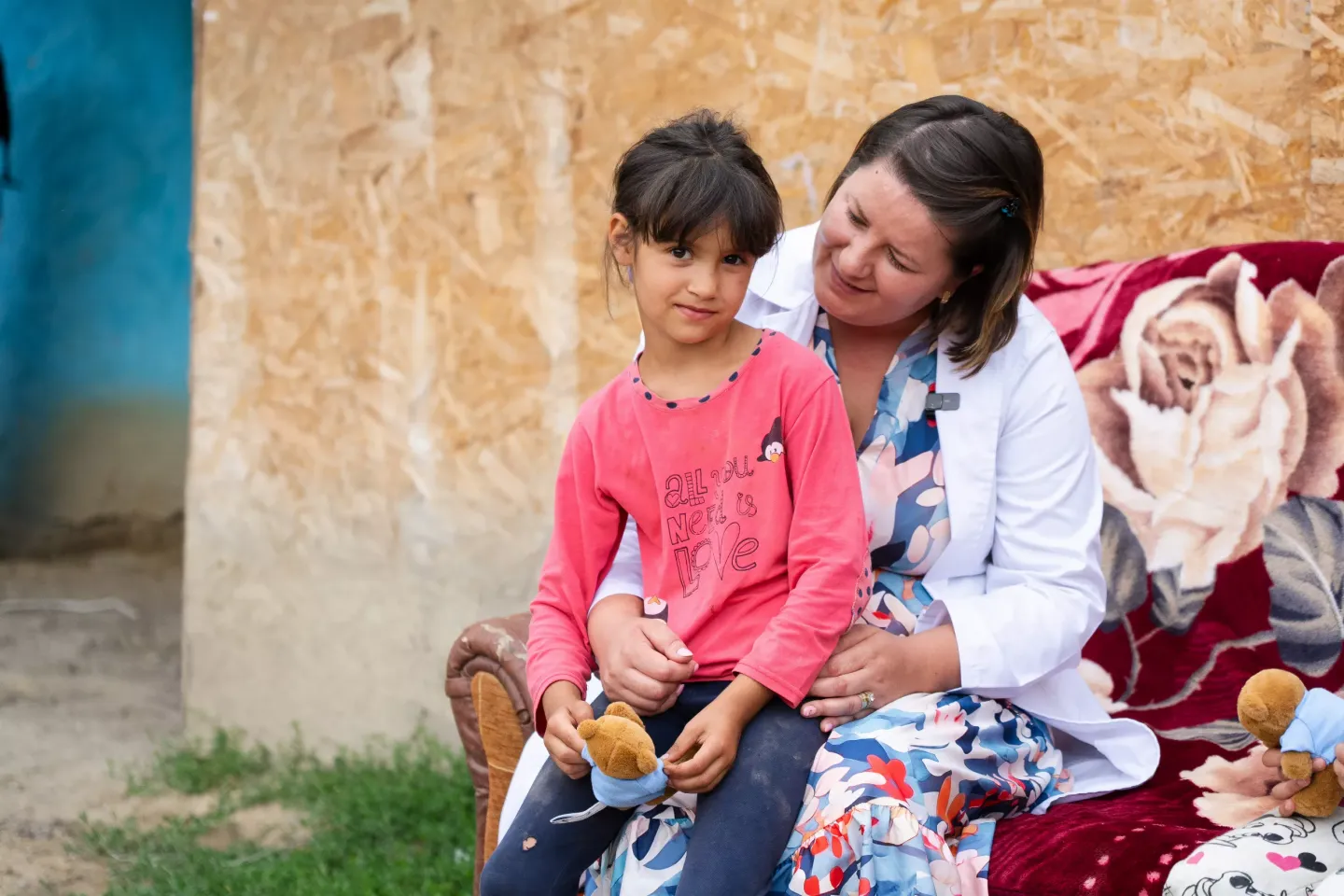 Asistent medical comunitar țin&acirc;nd &icirc;n brațe o fetiță pe canapea. 