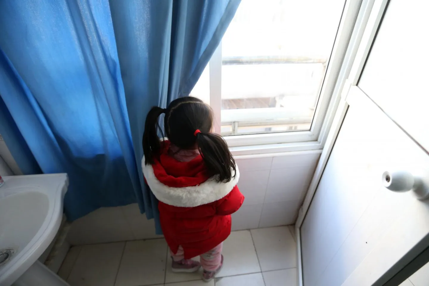 A girl in a red jacket looks through the window outside