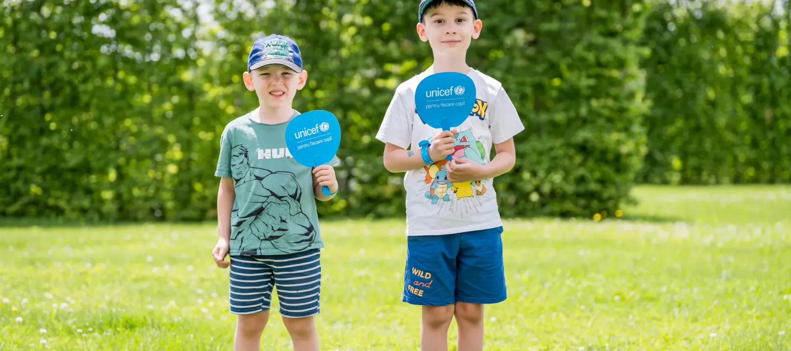 Two children being photographed while standing outside in a garden.