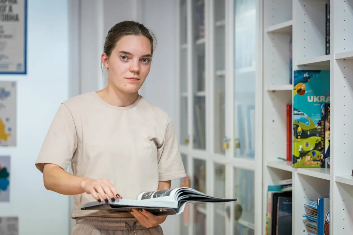 Young adolescent girl looking at the camera, while holding an open book in her hands.
