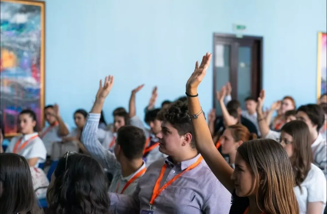 Grup de copii cu m&acirc;inile ridicate &icirc;n aer.