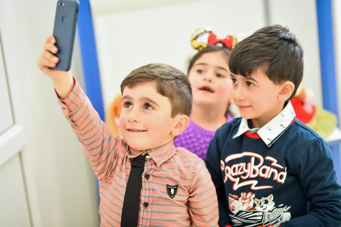 Group of three children looking at a phone that is held up in the air by one of them.