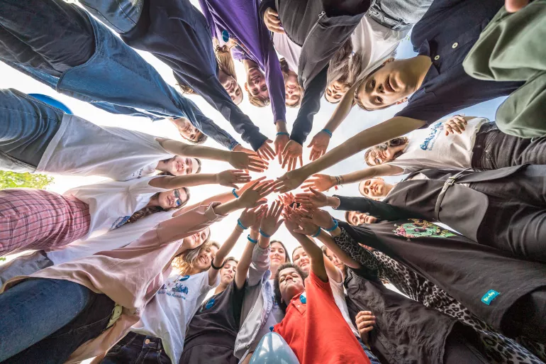 A group of children joining hands in a circle, photographed from below