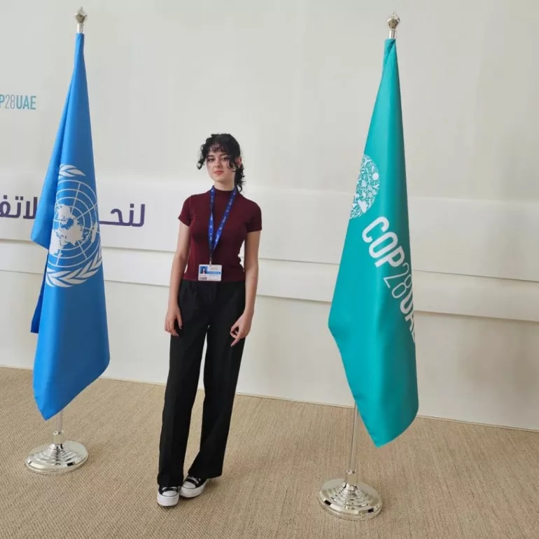 Teenage girl standing next to UN and COP28 flags